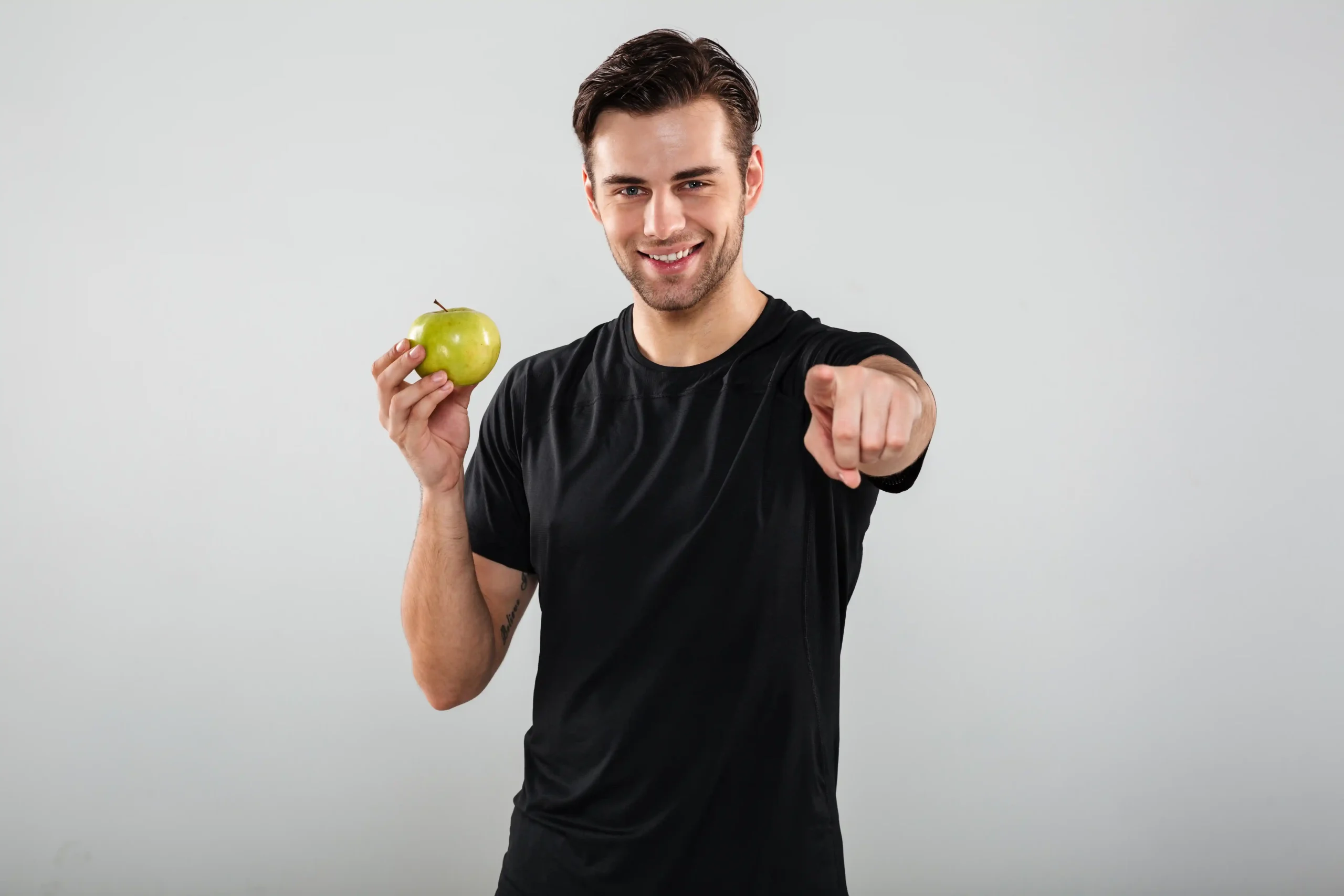 smiling-young-sports-man-holding-apple-pointing-you