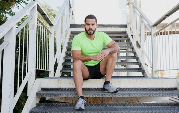 A man wearing a green shirt is sitting on a set of stairs, looking contemplative.