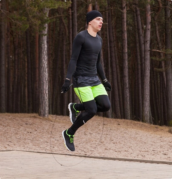 A man energetically jumps while using a skipping rope in an outdoor setting.