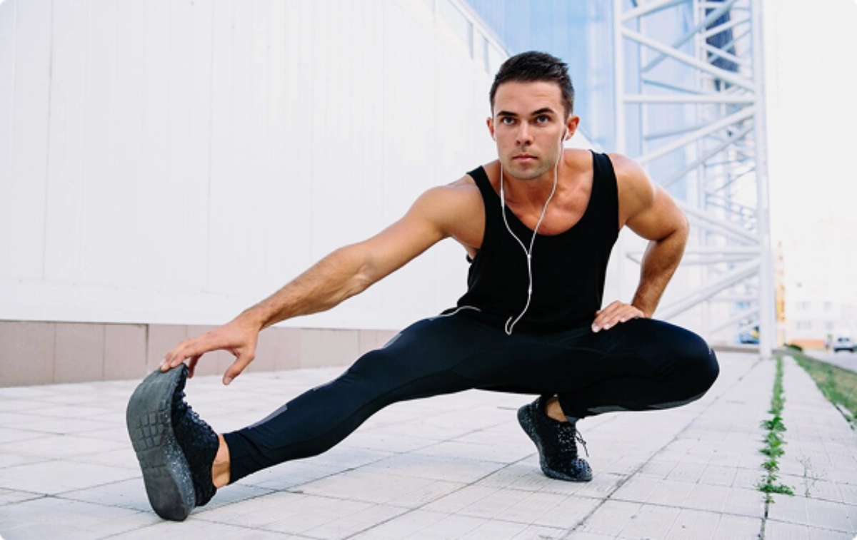A man stretches while wearing headphones, focusing on his fitness routine in a bright, open space.