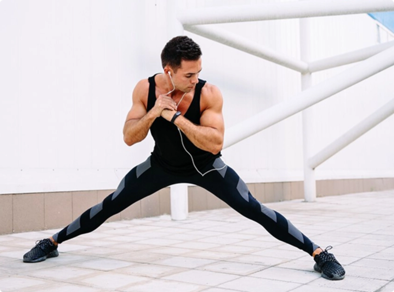 A man in a black tank top and pants stretches his body, focusing on flexibility and fitness.