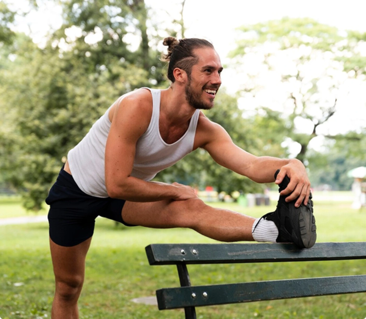 A man is stretching his arms and legs while seated on a bench in a park setting.
