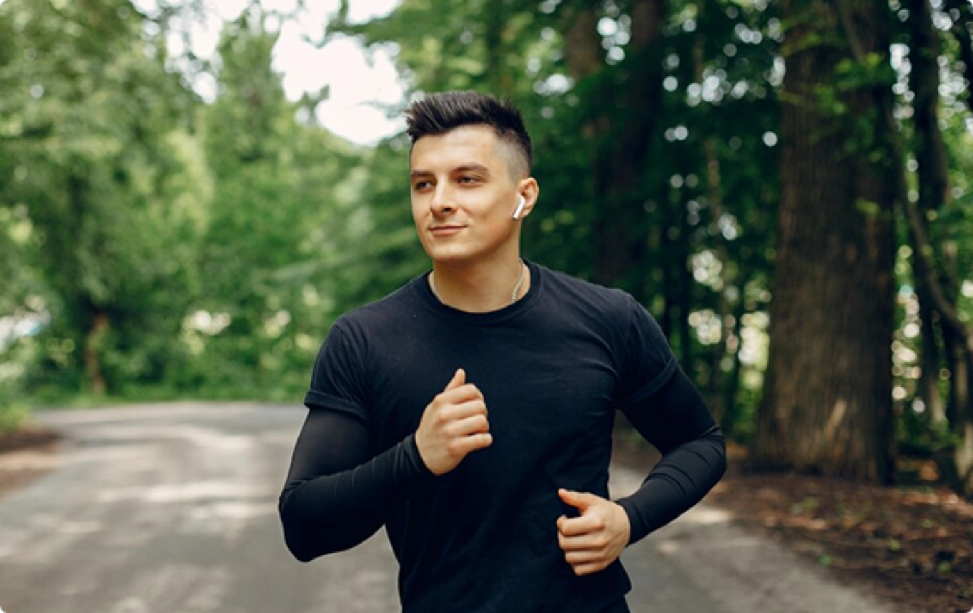 A man runs through a lush green forest, surrounded by tall trees and dappled sunlight filtering through the leaves.