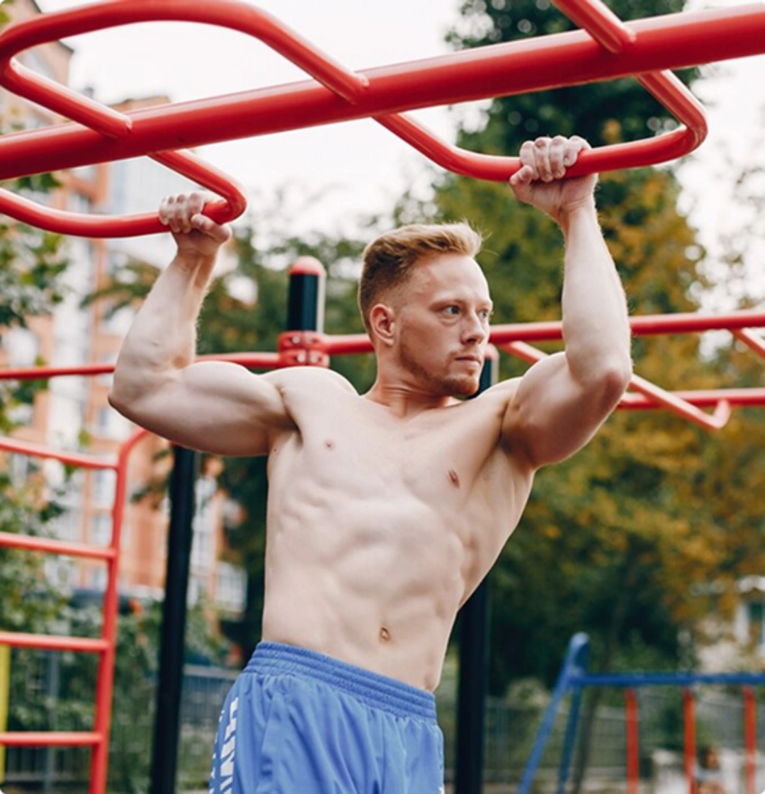 A shirtless man stands in front of a wooden fence, looking directly at the camera with a neutral expression.