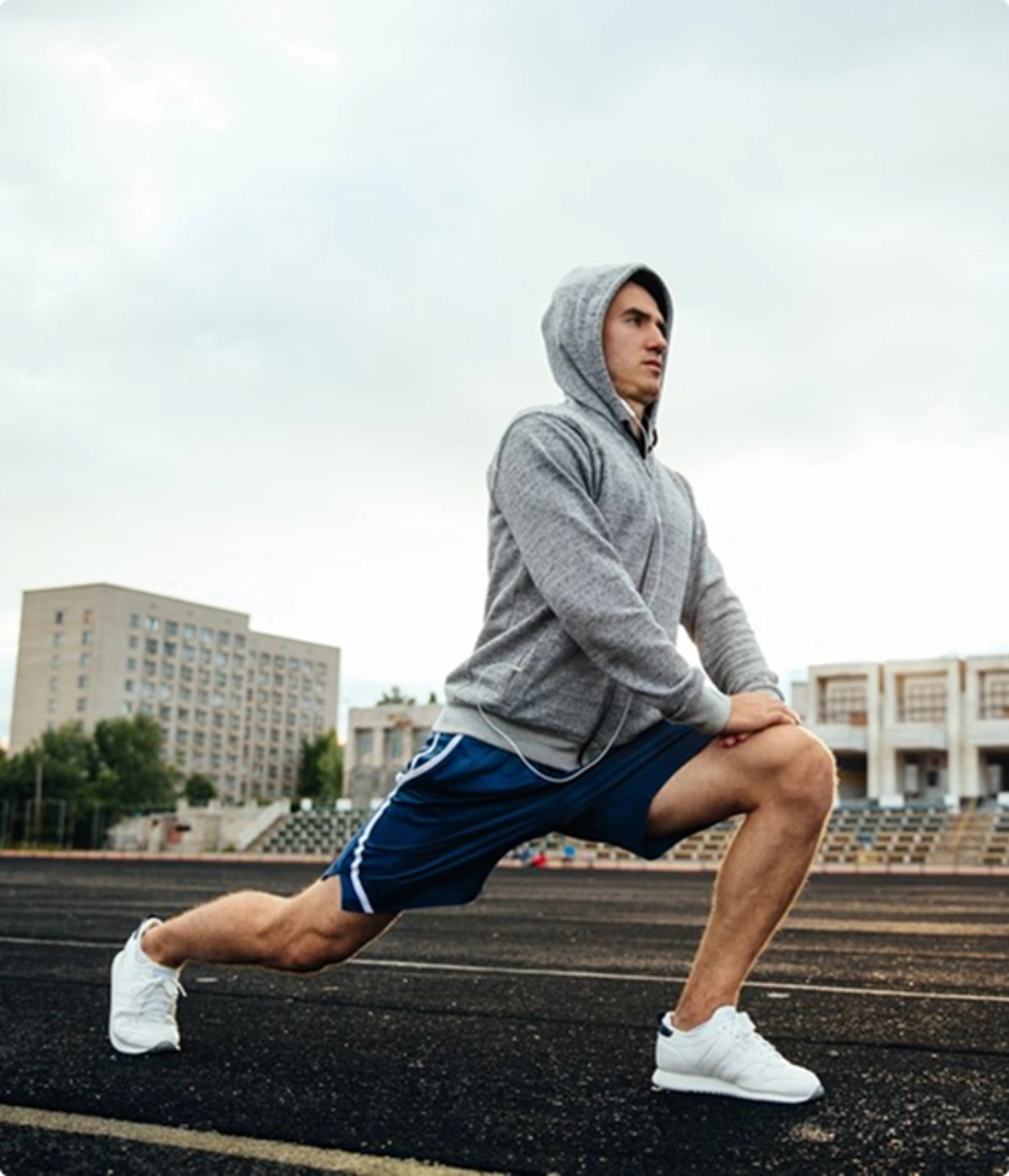 A man in a hoodie performs a squat, focusing on his form and balance in a gym setting.