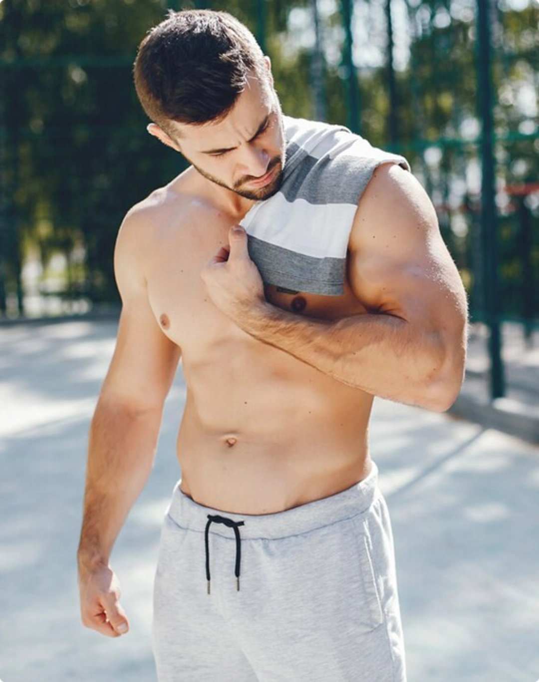A shirtless man stands confidently in front of a basketball court, ready for a game or practice.