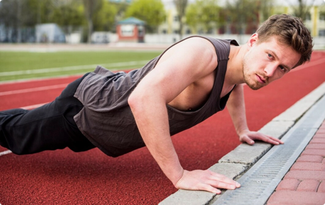 A man performing push-ups on a running track, demonstrating strength and fitness in an outdoor setting.