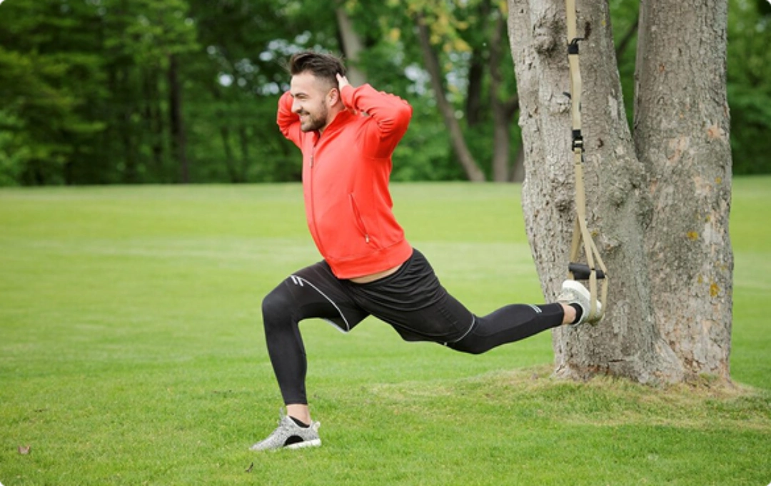 A man stretches his legs while holding onto a tree for support in a natural outdoor setting.